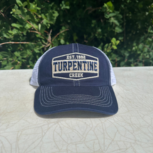 Load image into Gallery viewer, A navy blue trucker hat with a curved brim and white mesh back, featuring a front patch that reads 'EST. 1992 TURPENTINE CREEK'.

